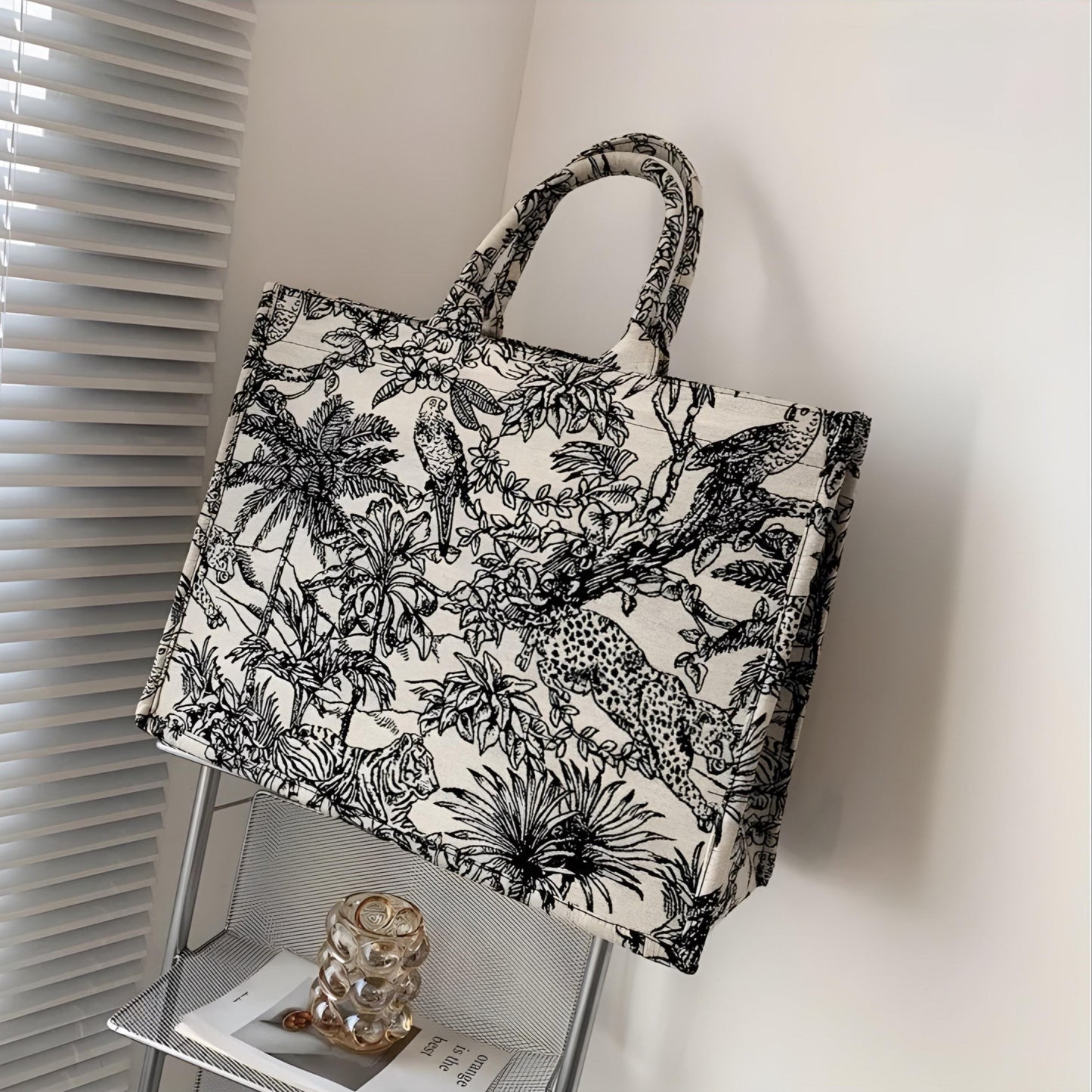 A white canvas tote bag with a black nature-themed print, displayed in a home setting.